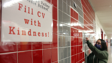 student putting note on Great Kindness Challenge wall