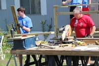 male sawing and other male carrying plank of wood