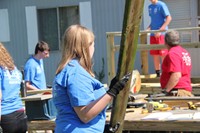 girl carrying plank of wood with people working on deck in background