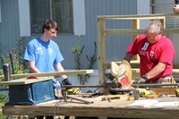 student helping man saw wood