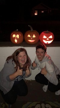 students smile in front of pumpkins they carved