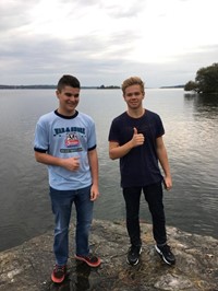 two male students smile standing on rock by water