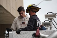 french student inside of bucket on fire truck with fire man