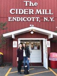 two female students smile in front of the cider mill