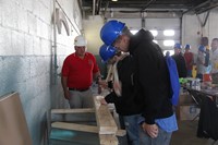two male students take on carpentry challenge of seeing who can hammer a nail into ply of wood quick