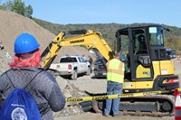 student watches other c v student use claw to lift rocks at construction career day