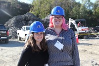 two female students smile in front of construction materials in the background