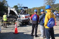 farther shot of students watching student pick up rocks using equipment at construction career day