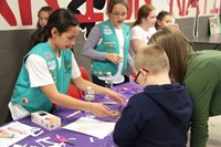 girl scouts helping student make harmonica at humanities night table