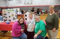 teacher smiles with boy and his grandma and mom at my little free library