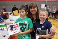 woman and two boys smile one boy holding american flag heart