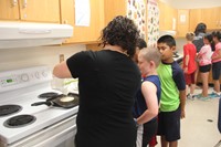 teacher helps students cook pancakes