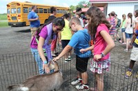 three students pet goat in pen.