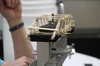 up close shot of bridge made of popsicle sticks going through test of how much weight it can hold