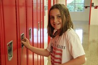 sixth grade student smiles standing next to her new locker at middle school orientation