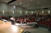 far away shot from front of auditorium of principal attleson speaking with sixth grade students pare