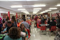 a wide shot from the back of the middle school cafeteria of incoming sixth graders and their parents