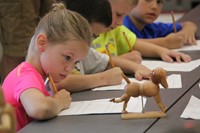 girl looks at wooden dog to sketch it