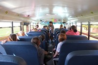 far shot from back of bus of bus driver talking to middle school students during bus drill