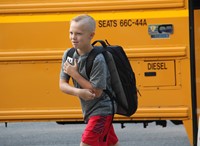boy smiles after getting off school bus walking towards elementary school on first day