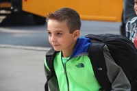 boy smiles walking towards elementary school on first day