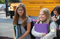 two girls smile walking towards elementary school on first day