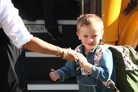 teacher gives student a hand to help him off the bus