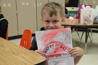 student holds up picture he colored that says happy first day of kindergarten