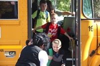 teacher greets students off bus on first day of school