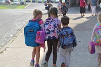 three students hold hands walking towards elementary school
