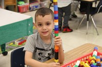 boy smiles next to lego tower he made on first day of school