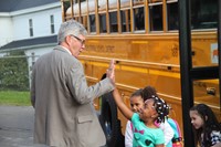 principal jim pritchard gives student a high five getting off the school bus