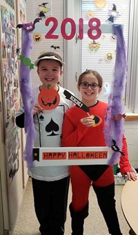 two students wearing costumes at photo booth sign in classroom