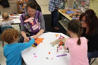 family members helping pre k students with scarecrow hats