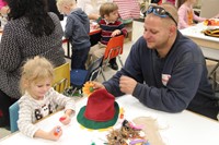 man helps student glue flower on hat at pre k family day