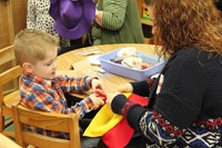 woman holds scarecrow hat while boy cuts with scissors