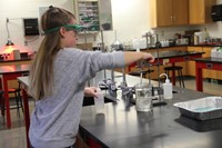 wide shot of student dipping ornament into liquid