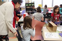 teacher watching student cut brown paper