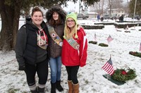 three girl scout members standing next to wreath on grave