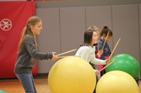 students hitting large exercise balls with drum sticks