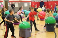 students hit drum sticks against exercise balls next to them