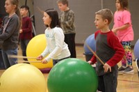 medium shot of students hitting drum sticks on large exercise balls