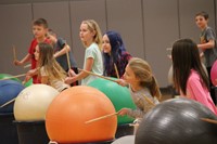 additional students hitting drum sticks on large exercise balls
