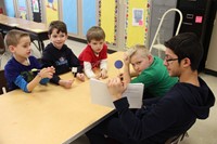 high school student reading book as four elementary students listen