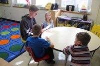 high school student reading book to three elementary students