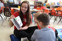 high school student reading book to two elementary students