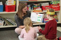 high school student reading her story to two elementary students