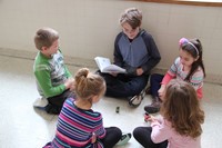 high school student reading his book to four elementary students