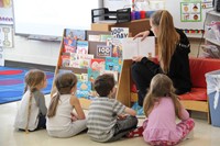 high school student reading to elementary students sitting