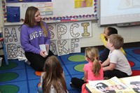 high school student reading to four elementary students